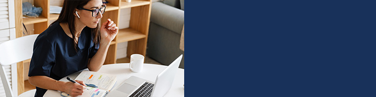 Woman wearing earbuds taking notes while looking at a laptop at a table.